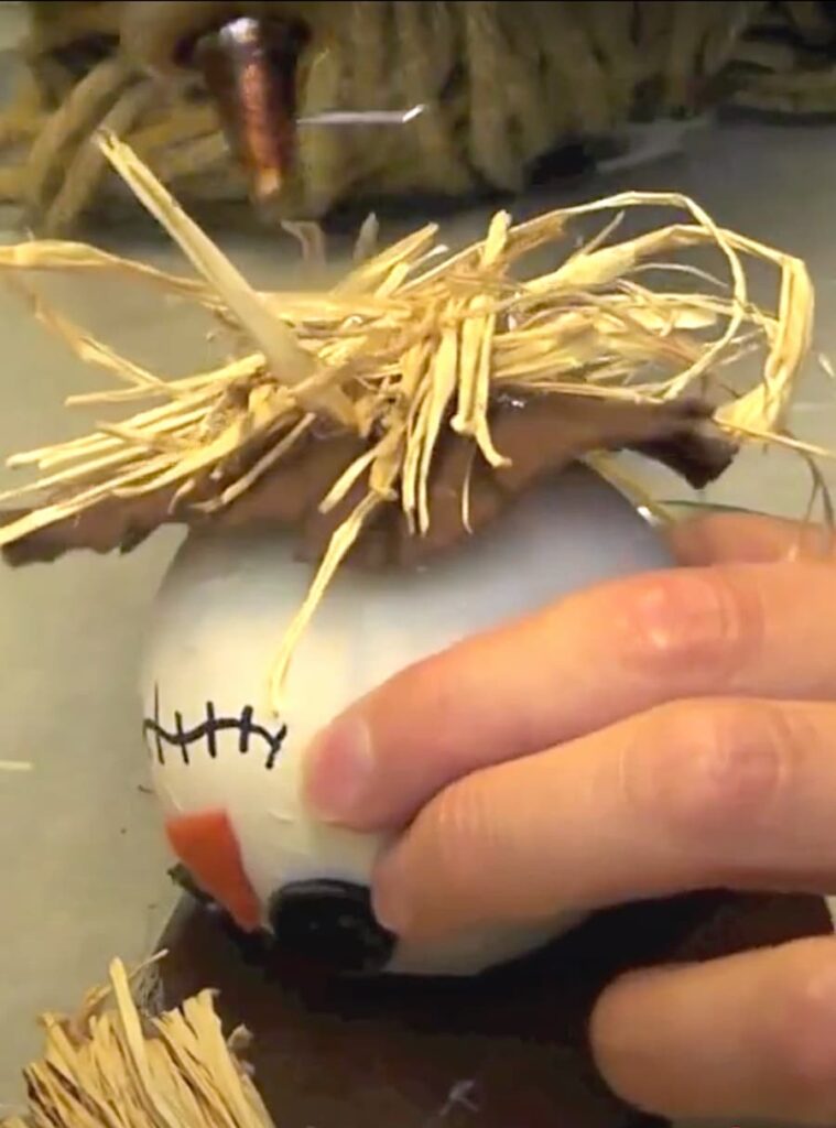 Gluing raffia under the collar of the scarecrow ornament craft