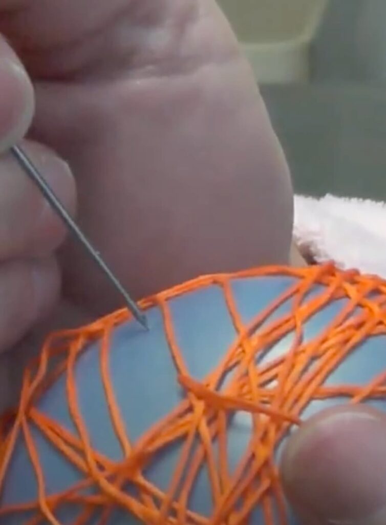 Using needle to pop balloon wrapped in orange embroidery floss