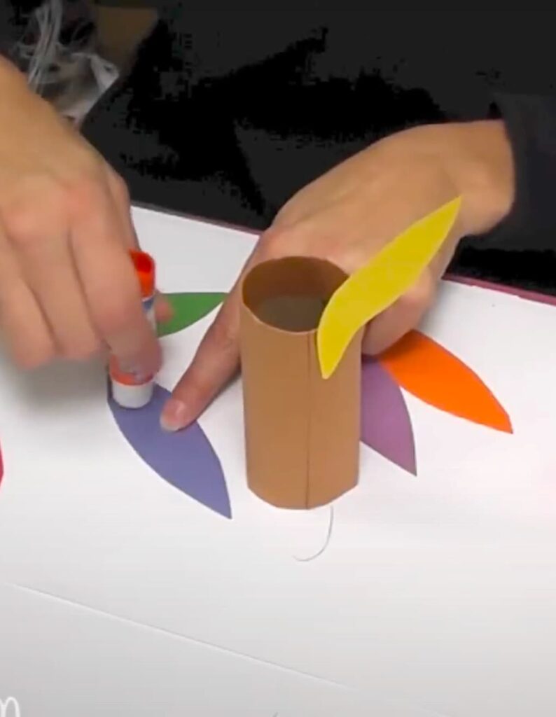 Gluing colorful turkey construction paper craft feathers onto the body