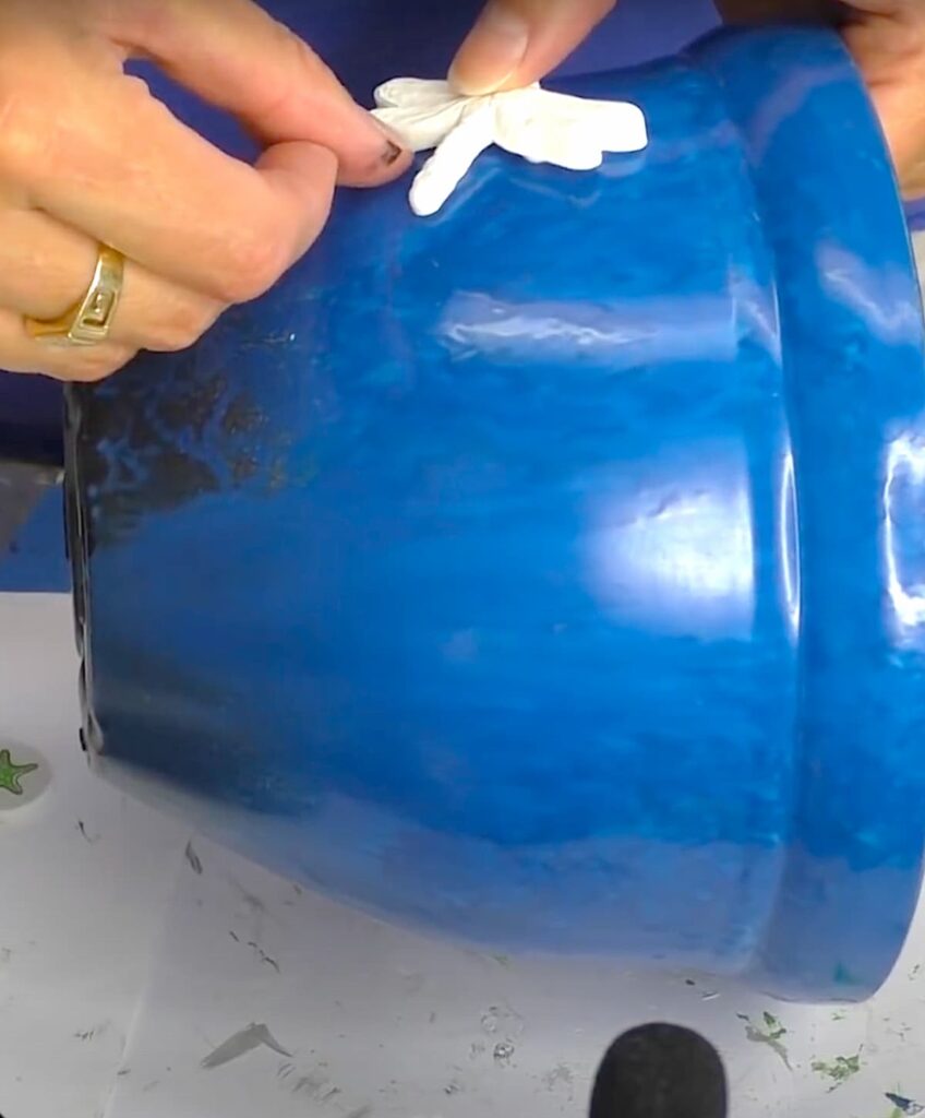 Gluing dragonfly on the side of blue flower pot