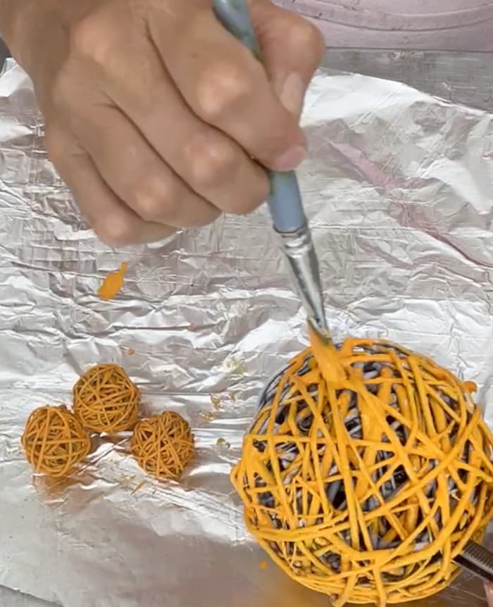 Painting twine balls orange  to turn them into pumpkins for the fall gnome scarecrow decoration 