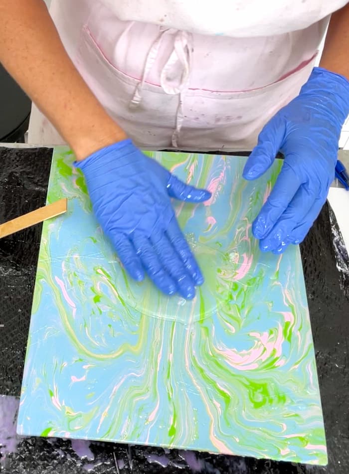 Spreading resin with gloved hands over the acrylic paint pour canvas