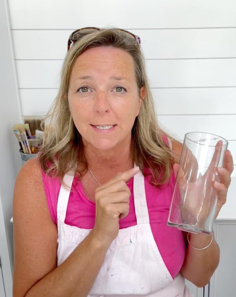 woman in a pink shirt and apron pointing to a glass vase