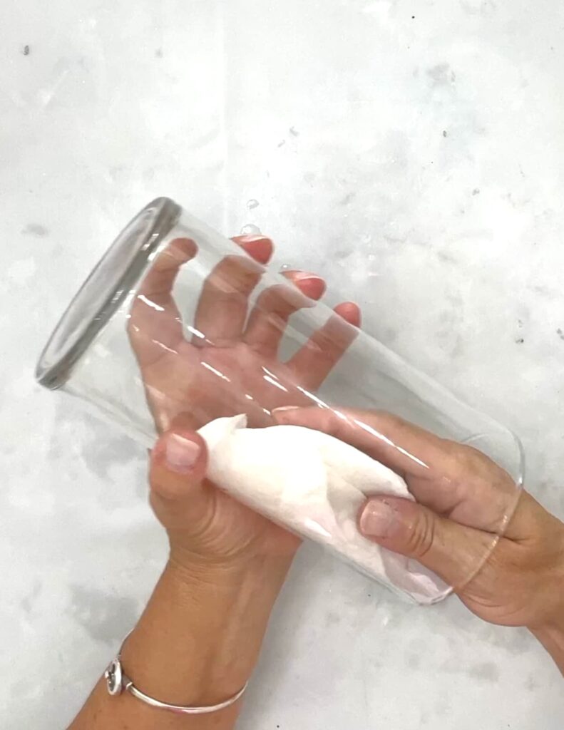 Hands cleaning the inside of a cylinder vase with a paper towel