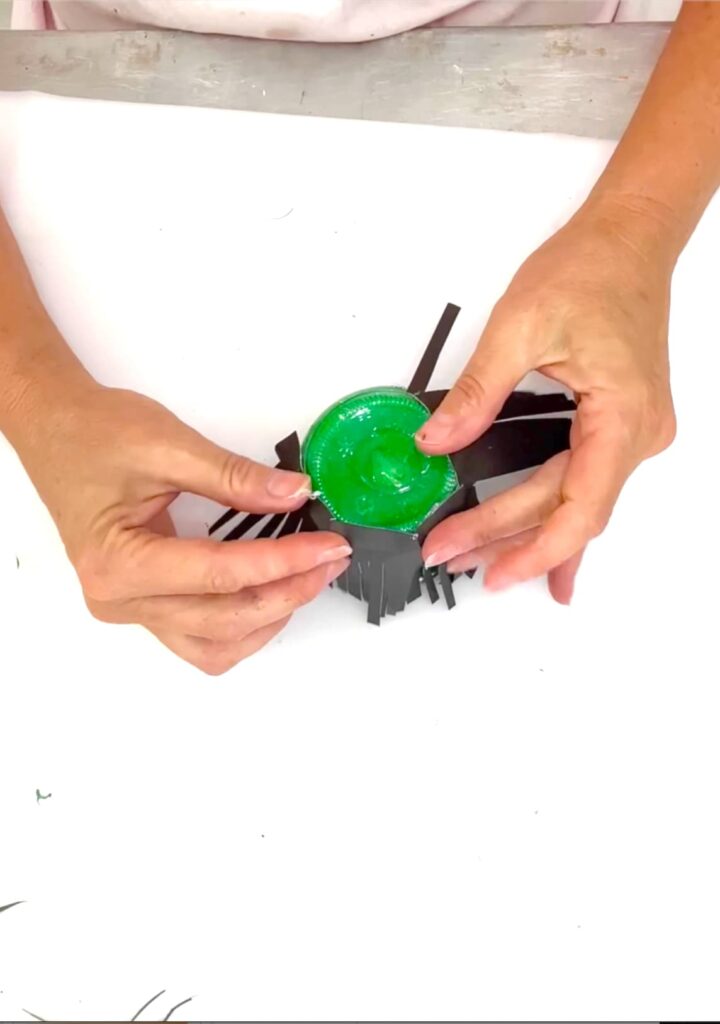 gluing black fringed card stock on a green jar for witch hair