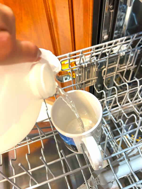 Pouring vinegar into a mug on top shelf of dishwasher