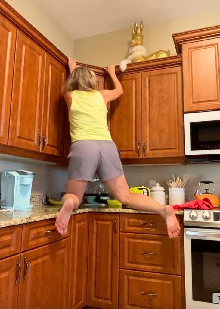 Woman climbing onto kitchen countertops to show how to clean kitchen cabinets